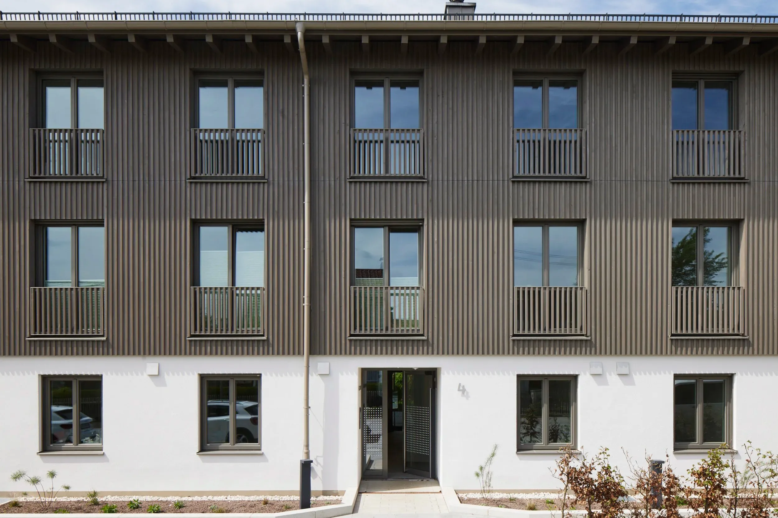 Straßenansicht mit Holzlamellenfassade und Balkonen