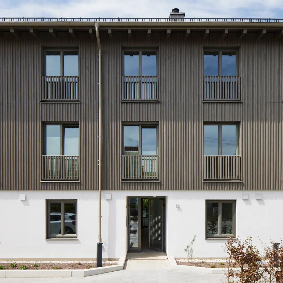 Straßenansicht mit Holzlamellenfassade und Balkonen