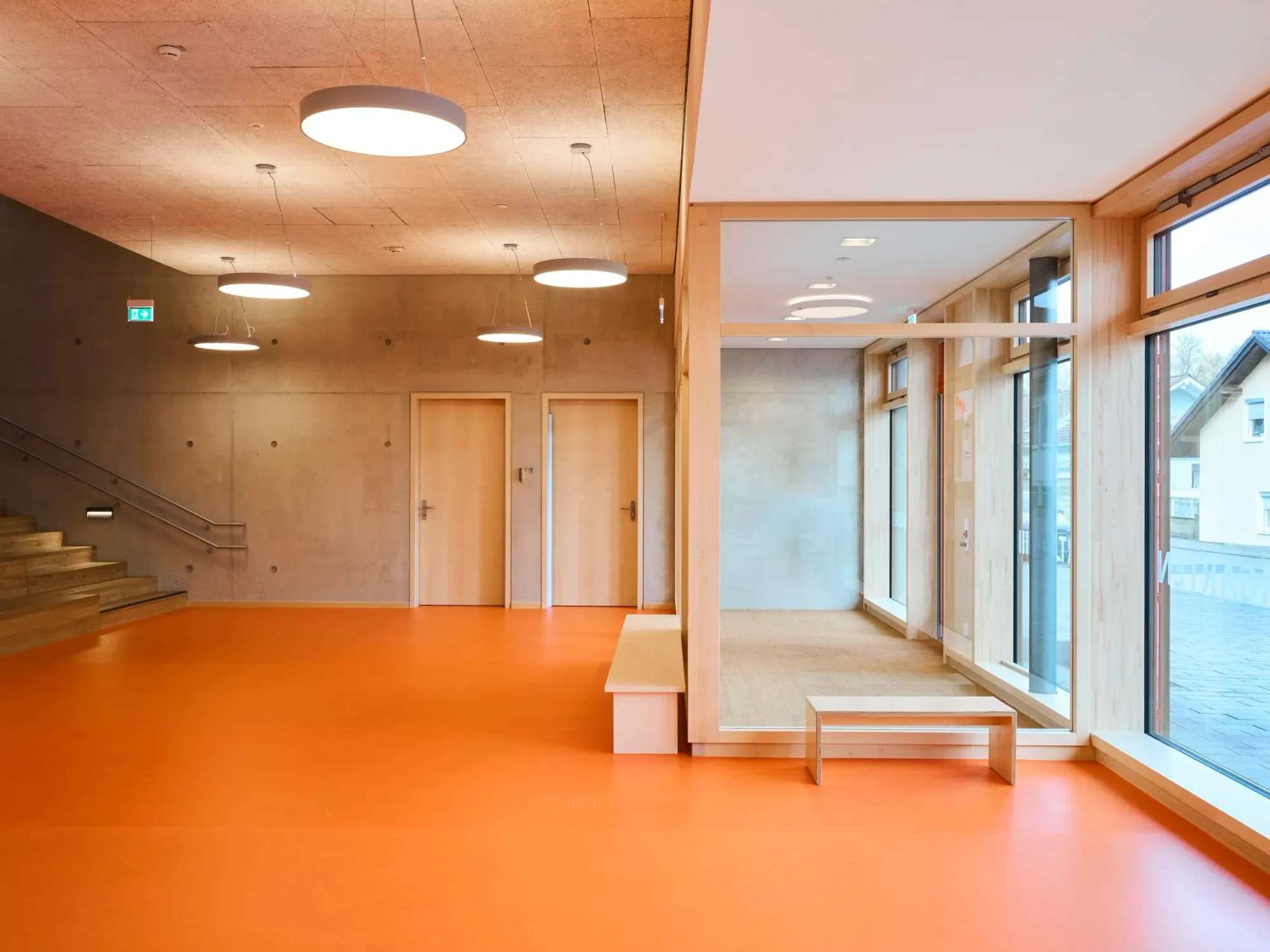 Foyer mit orangem Boden, Sitzstufen und Blick in den verglasten Gruppenraum