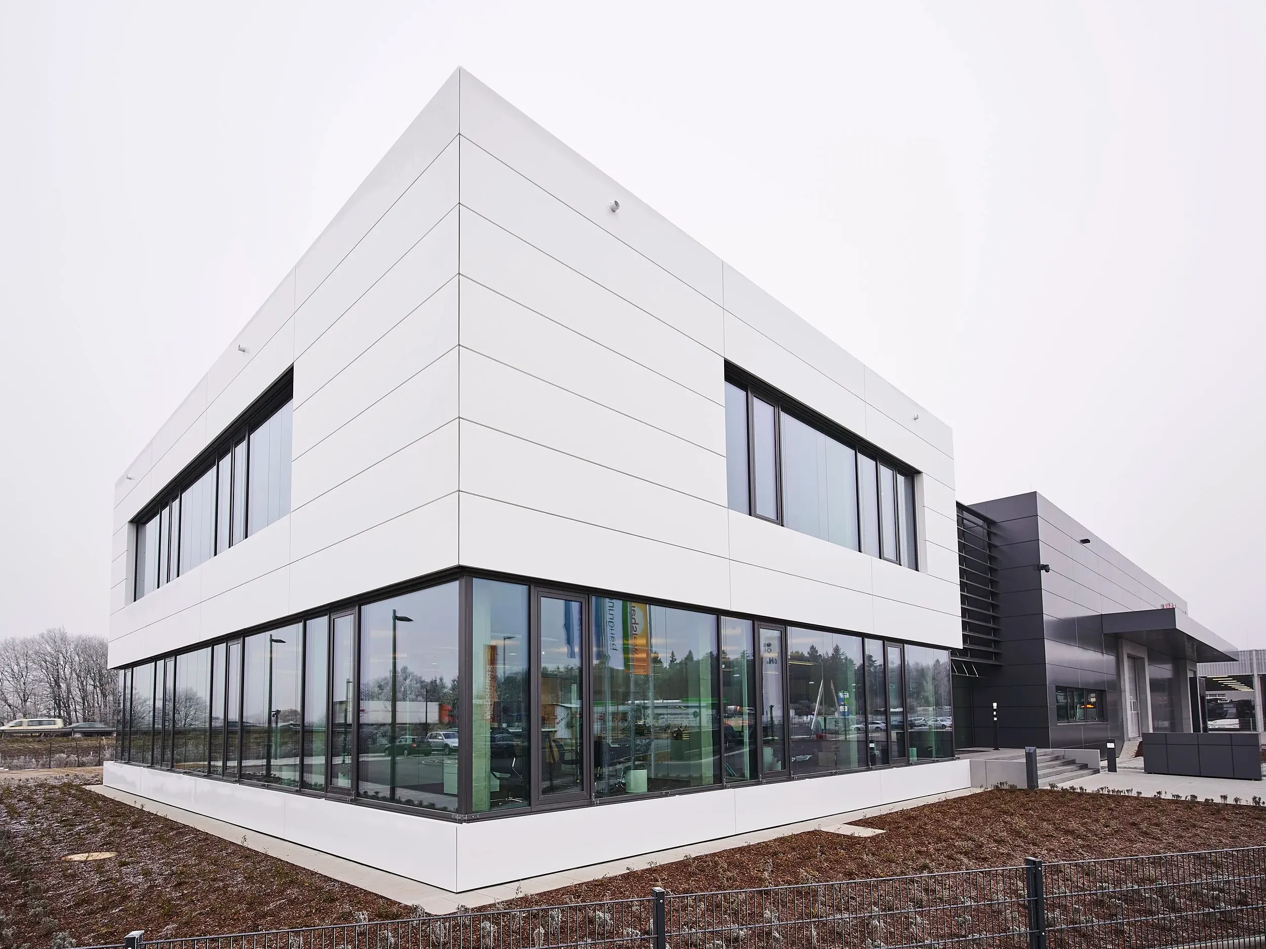 Eckansicht mit verglastem Erdgeschoss und Lagerhalle im Hintergrund