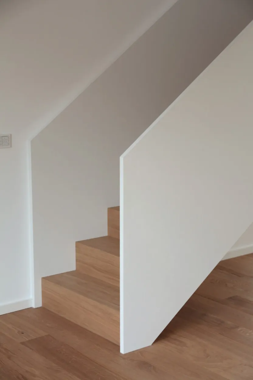 Treppe mit Holzstufen hinter einer weißen, schräg geschnittenen Brüstungswand, Holzboden