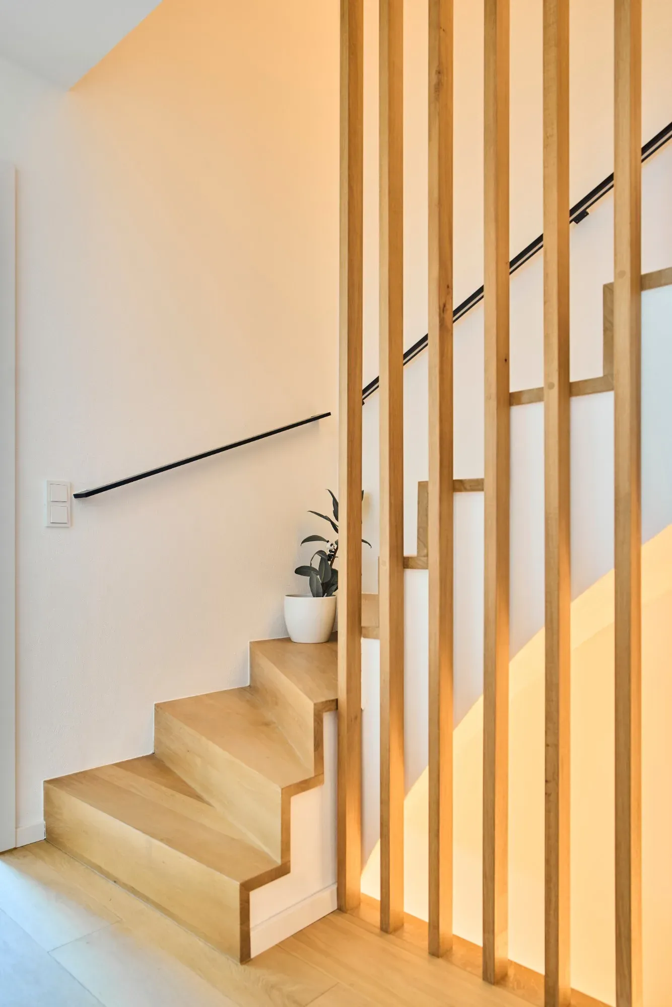 Holztreppe hinter senkrechten Eichenstäben, schwarzer Handlauf an der Wand