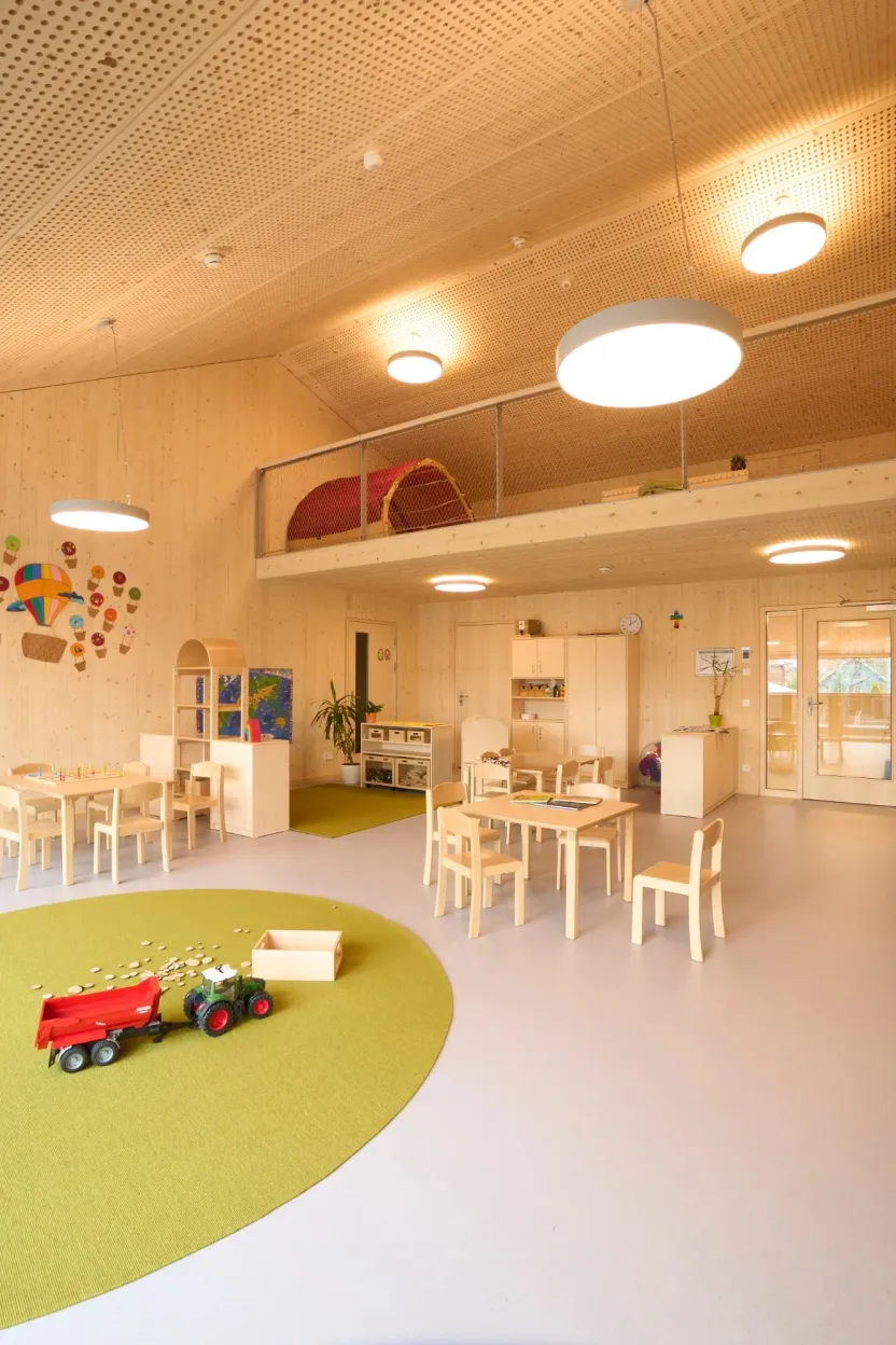 Gruppenraum mit Holzwänden, gelochter Holzdecke, Galerie und grünem Teppich