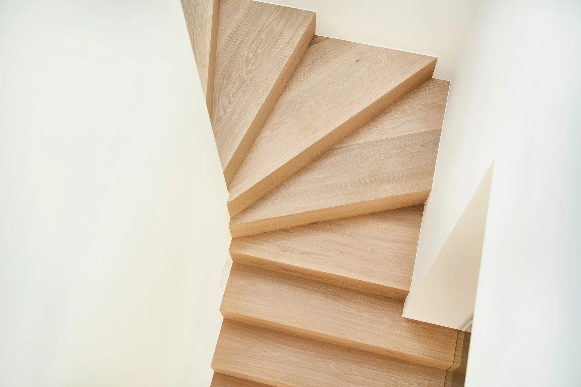 Gewendelte Treppe mit Eichenstufen zwischen weißen Wänden, von oben gesehen