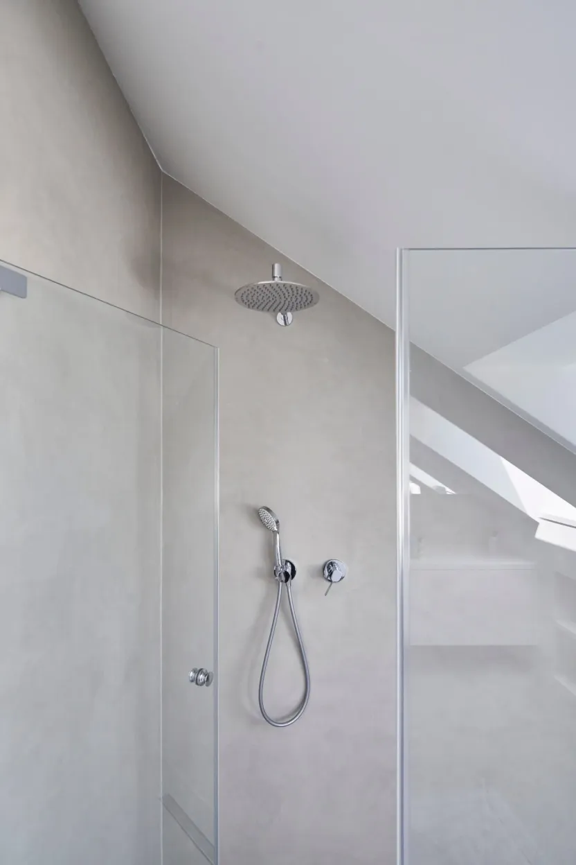 Dusche unter der Dachschräge mit Regen- und Handbrause, fugenlose graue Wand und Glastüren