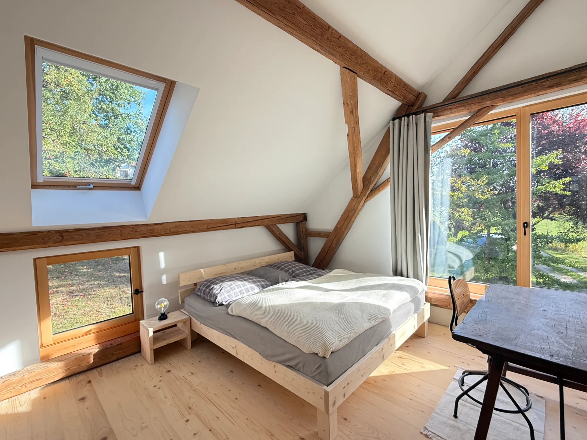 Schlafzimmer mit Holzbalken, Dachfenster, Bett und Gartenausblick
