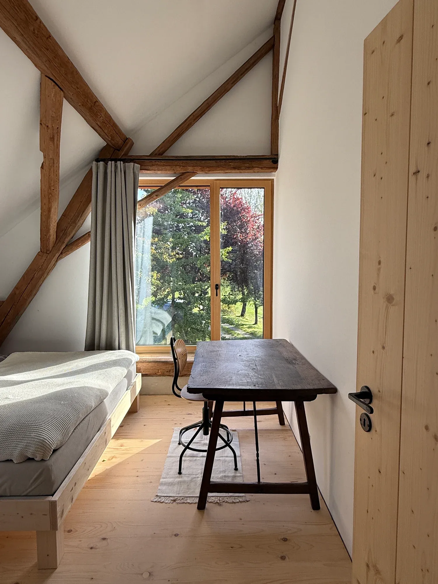 Schlafzimmer mit Bett, Schreibtisch und bodentiefem Fenster