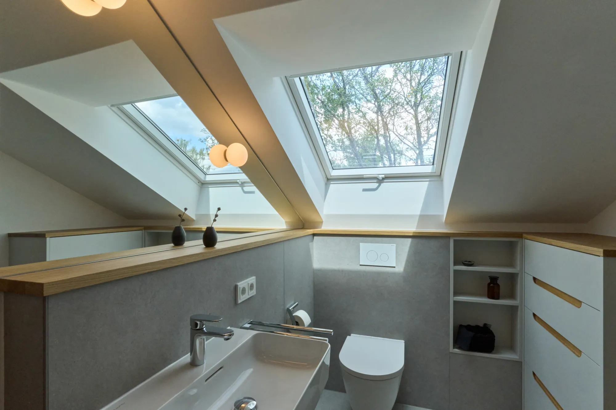 Badezimmer unter der Dachschräge mit großem Spiegel, Dachfenster, Waschtisch und Einbauschrank mit Holzgriffen