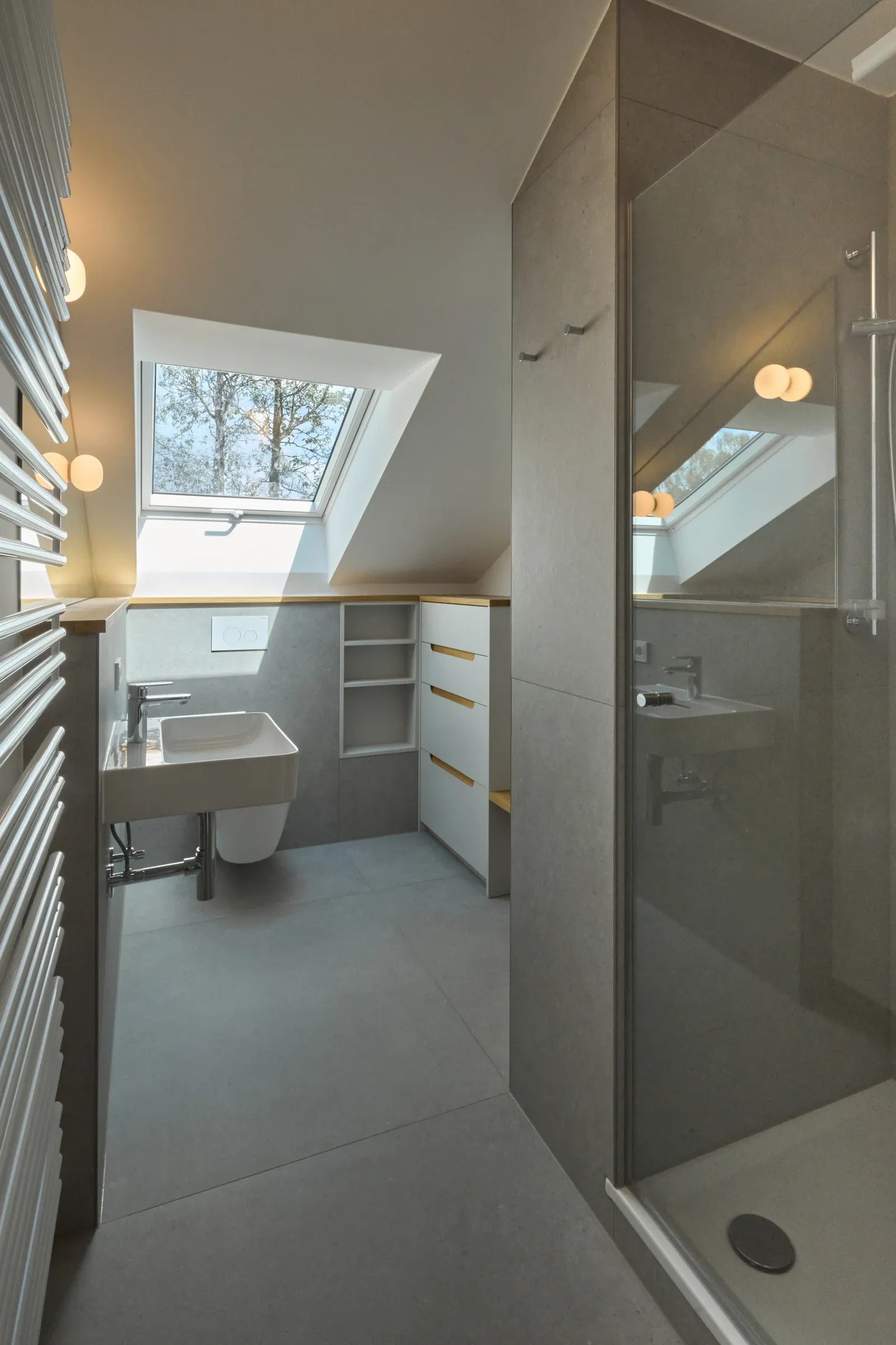 Blick ins Badezimmer mit verglaster Dusche, Waschtisch und maßgefertigtem Stauraum unter dem Dachfenster