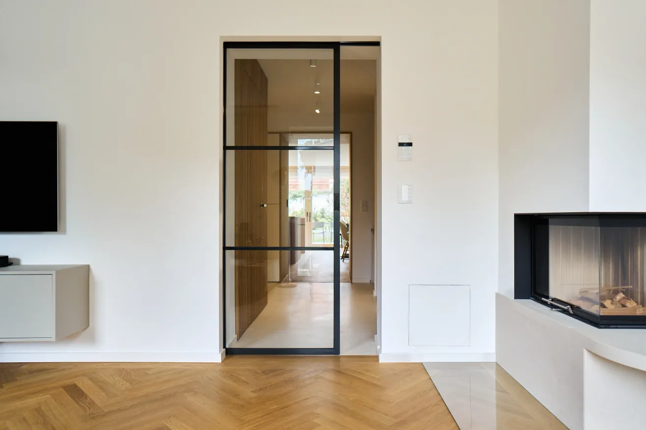 Glastür mit schwarzem Rahmen zwischen Wohnzimmer und Flur neben einem Eckkamin