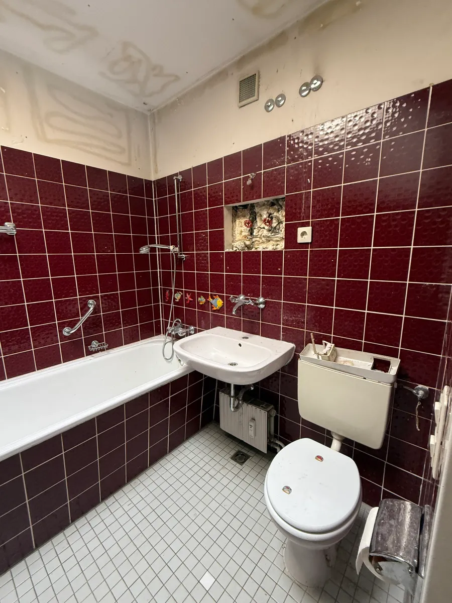 Bad im Bestand mit dunkelroten Wandfliesen, Badewanne und Waschbecken