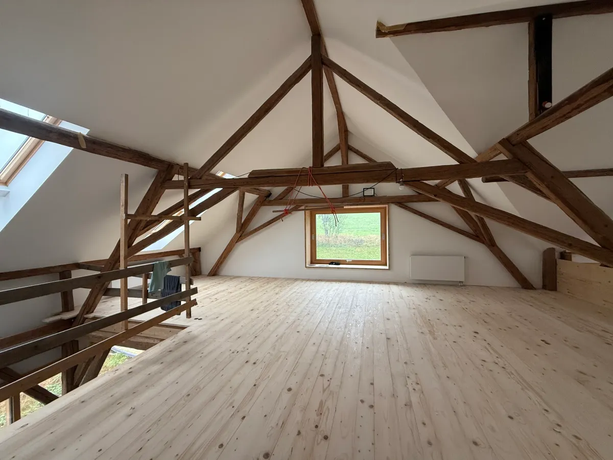 Blick über die Fichtendielen auf das historische Holztragwerk und das Fenster im Dachraum