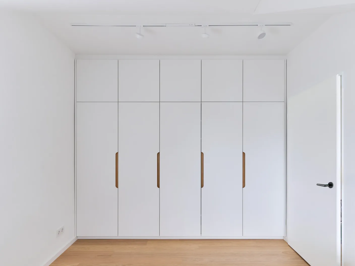 Wandfüllender Einbauschrank im Schlafzimmer mit geschlossenen weißen Türen und Griffmulden aus Holz