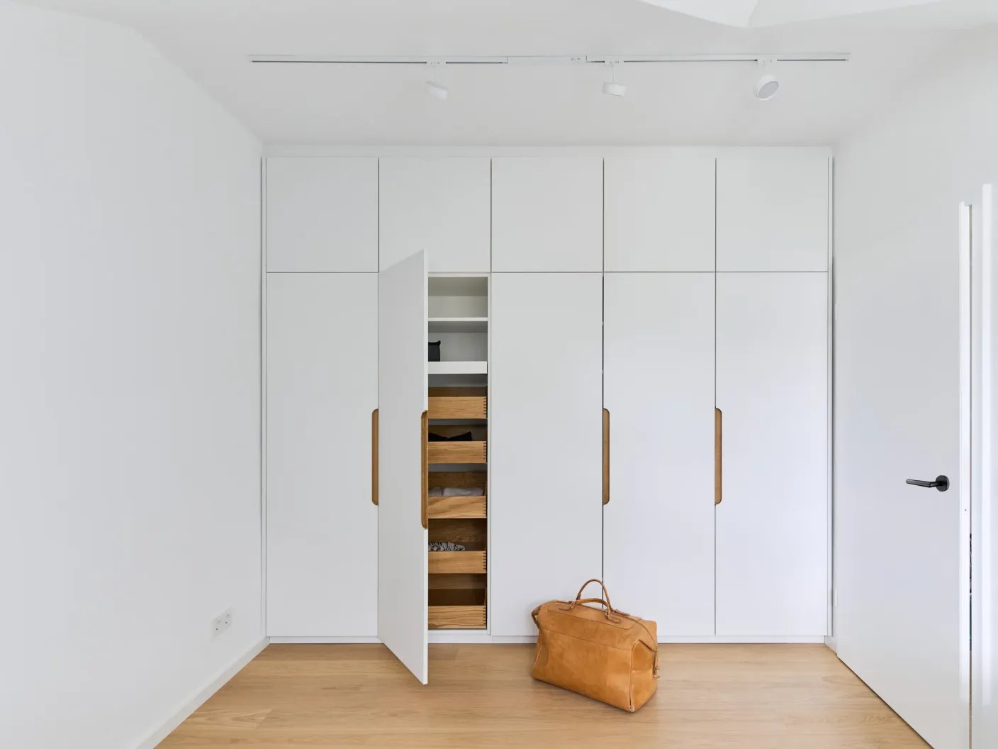 Einbauschrank im Schlafzimmer mit geöffneter Tür, weißen Regalfächern und hölzernen Schubladen